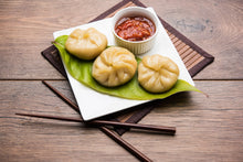 Load image into Gallery viewer, Beautifully platted momos served with chutney which is kept upon a dinning mat with some chopsticks aside.
